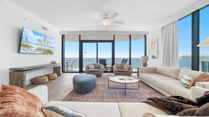 A spacious living room with a large window, a ceiling fan, and a view of the ocean. - Unreal Views from this Beachfront 4BR Beauty! (Gulf Shores)