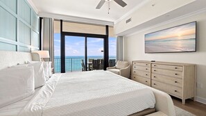 Ein geräumiges Schlafzimmer mit einem großen Bett, einem Schminktisch, einem Sessel und einem Balkon mit Meerblick.