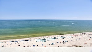 Une plage bordée de rangées de parasols et de chaises longues, un rivage sablonneux et l’océan en toile de fond.