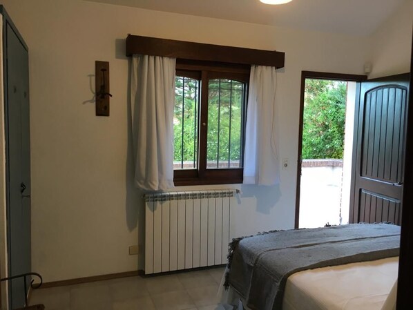 A bedroom with a window, a radiator, and a door leading outside.