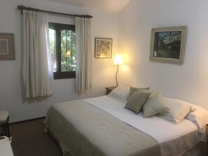 A bedroom with a bed, a nightstand, a lamp, a window with curtains, and two framed pictures on the wall.