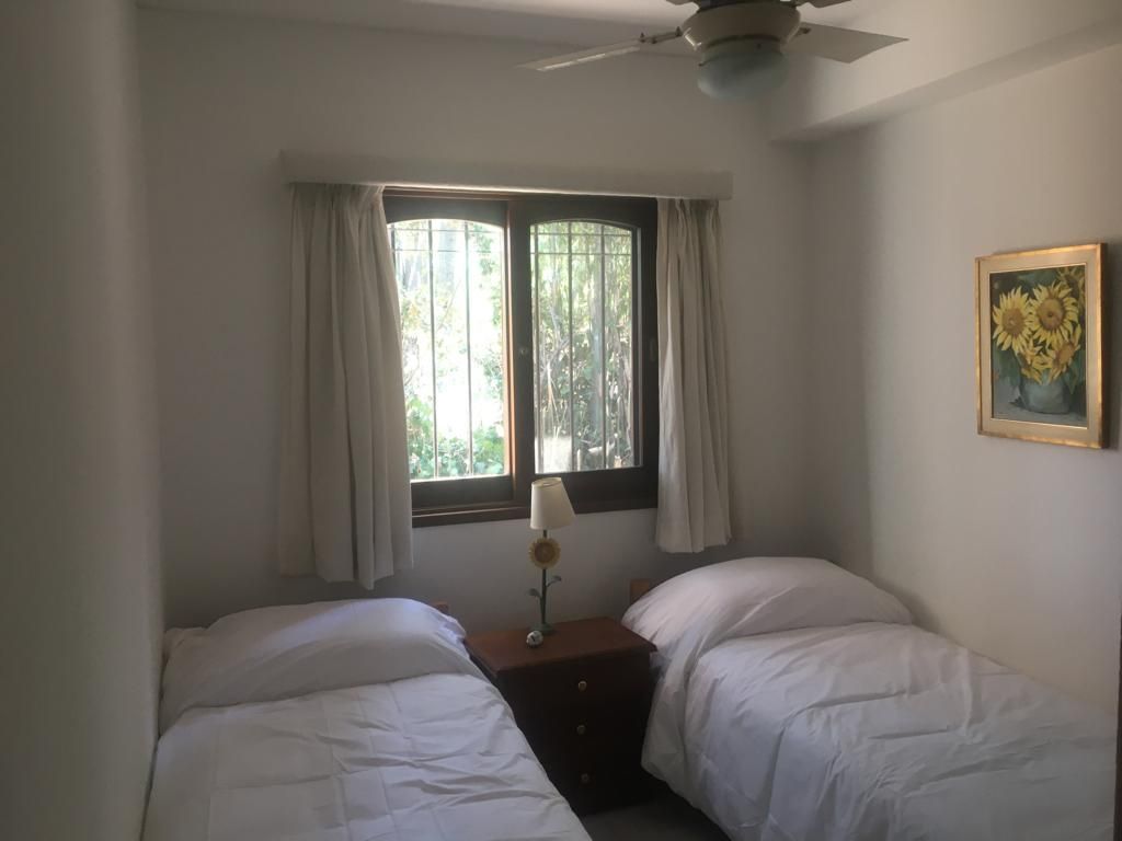 A room with two beds, a window with curtains, a ceiling fan, and a framed picture on the wall.