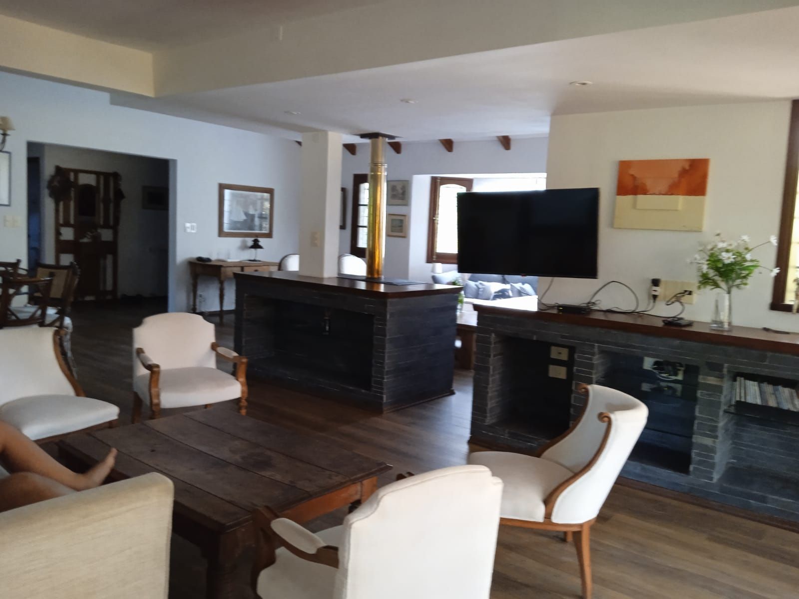 A spacious living room with a fireplace, a television mounted on the wall, and a dining area with wooden furniture.