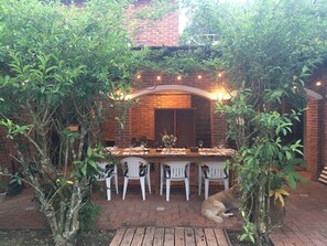 An outdoor dining area with a brick wall, a wooden table set for four, and white chairs.