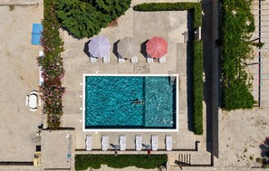Eine Vogelperspektive auf einen Poolbereich mit angrenzenden Liegestühlen und Sonnenschirmen.