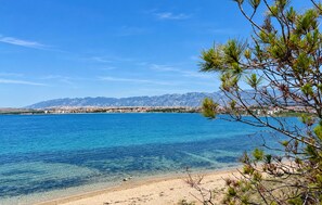 Eine Küstenlandschaft mit klarem, blauem Wasser, einem Sandstrand und einer Bergkette im Hintergrund.