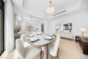 A modern dining area with a round table set for four, a chandelier, and a 'BOOK ME' sign on the wall. - StayShort - Fabulous 2-Bedroom at Al Tajer in Downtown with Easy Access to Dubai Mall (Downtown Dubai)
