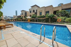A swimming pool with lounge chairs and a lifebuoy, surrounded by greenery and a building with a tiled roof. - StayShort - Fabulous 2-Bedroom at Al Tajer in Downtown with Easy Access to Dubai Mall (Downtown Dubai)
