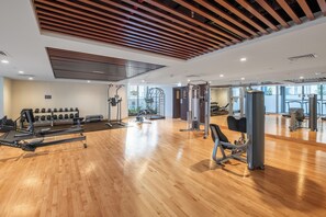 Ein Fitnessraum mit unterschiedlichen Trainingsgeräten, Holzböden und großen Fenstern.