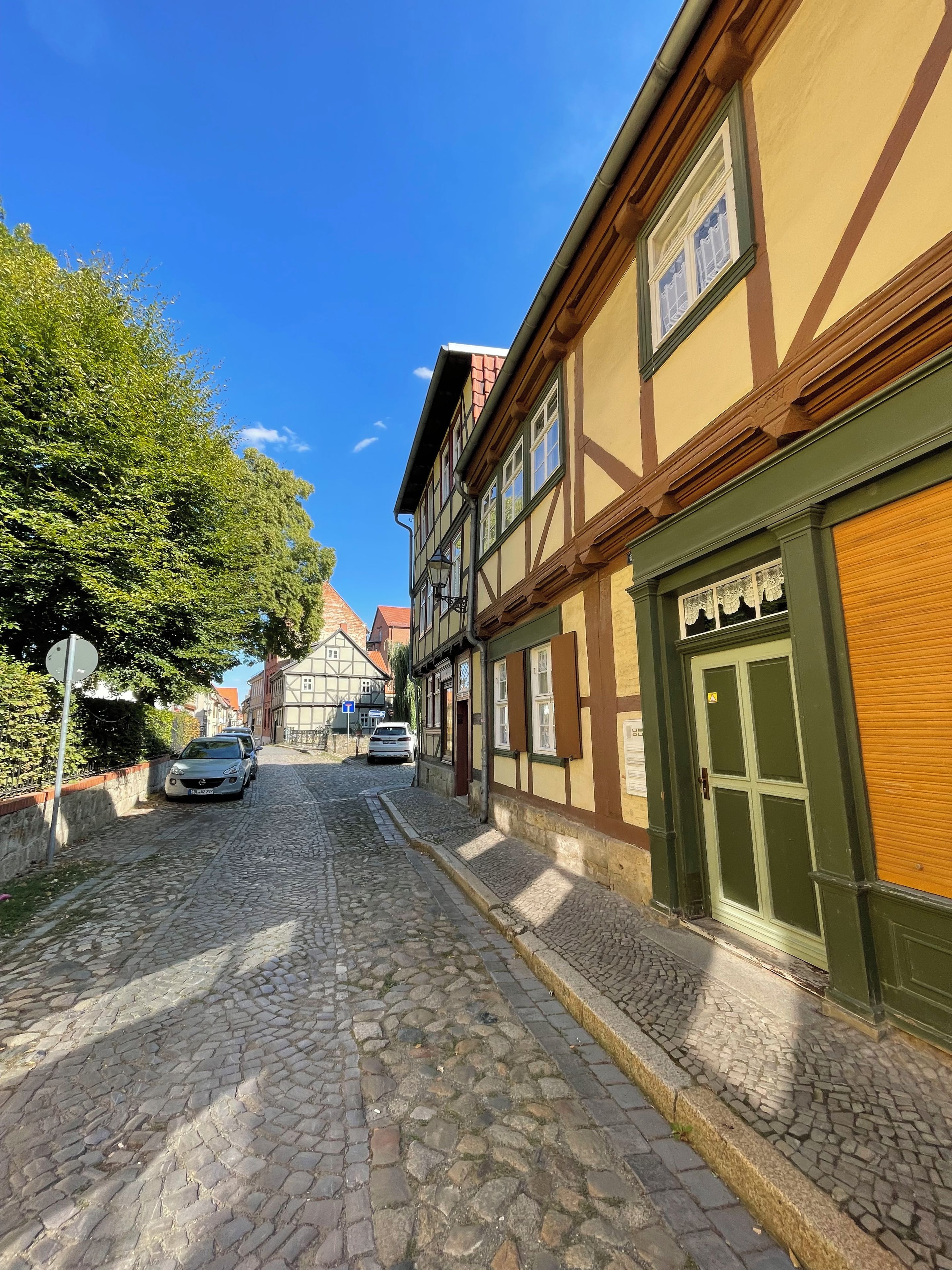 Eine Kopfsteinpflasterstraße gesäumt von traditionellen Fachwerkhäusern, mit blauem Himmel und geparkten Autos.