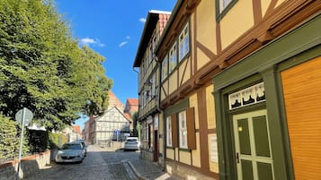 Eine Kopfsteinpflasterstraße gesäumt von traditionellen Fachwerkhäusern, mit blauem Himmel und geparkten Autos.
