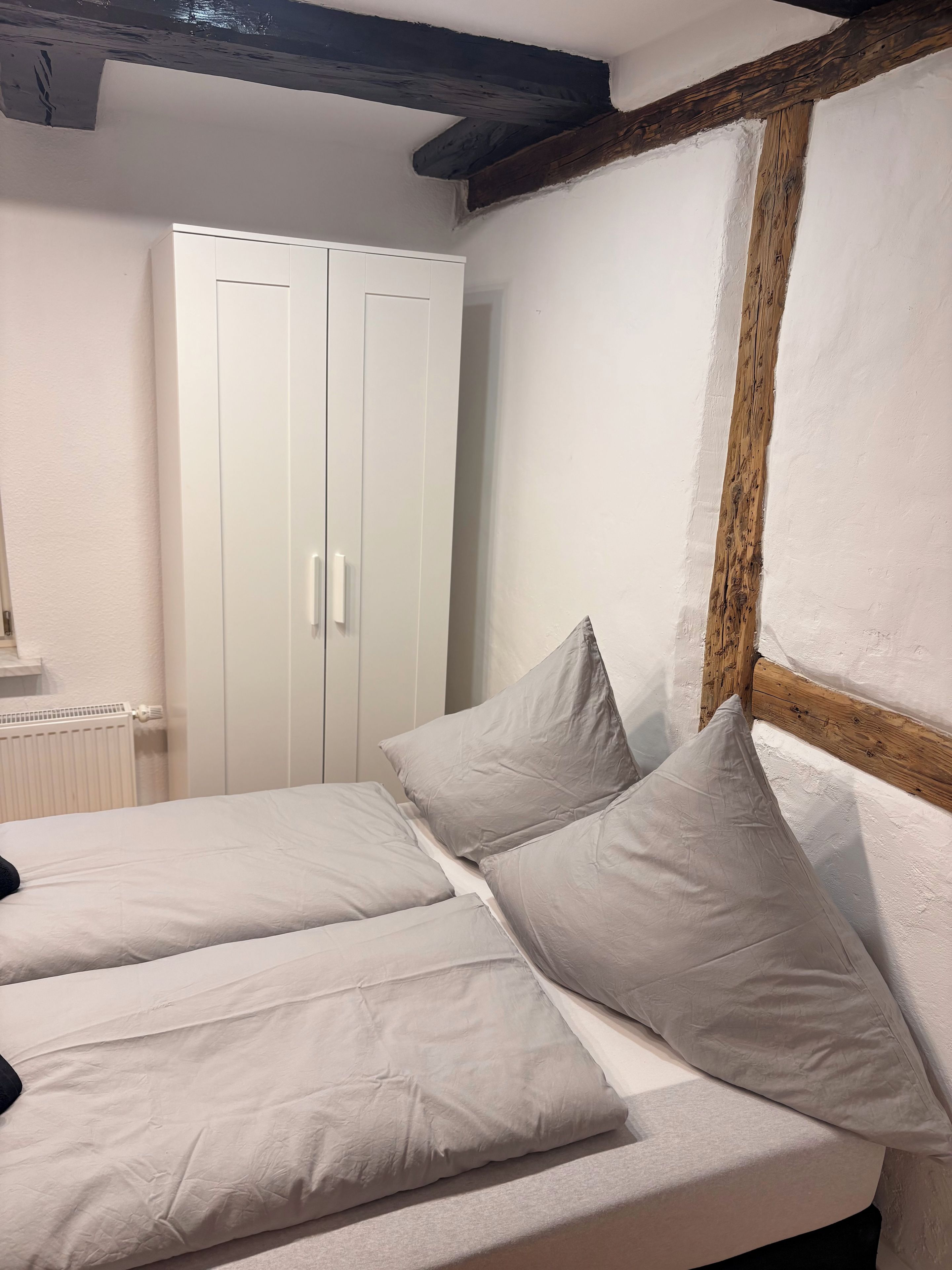 A bedroom with a bed, white wardrobe, and exposed wooden beams.