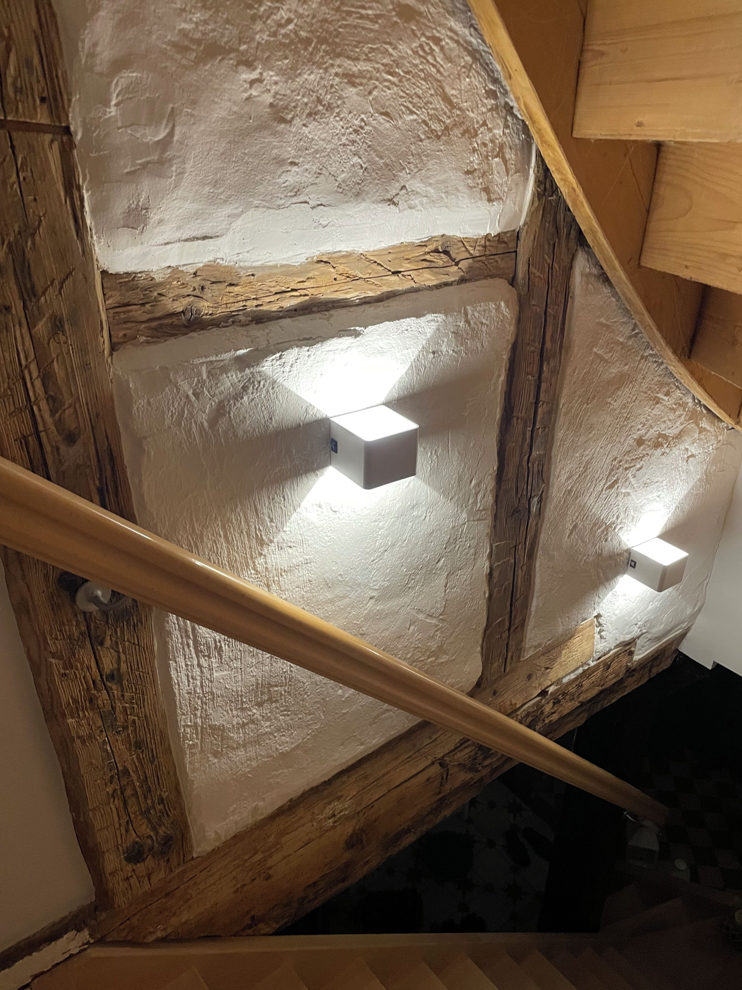 A staircase with wooden railings and a white wall with two recessed lights.