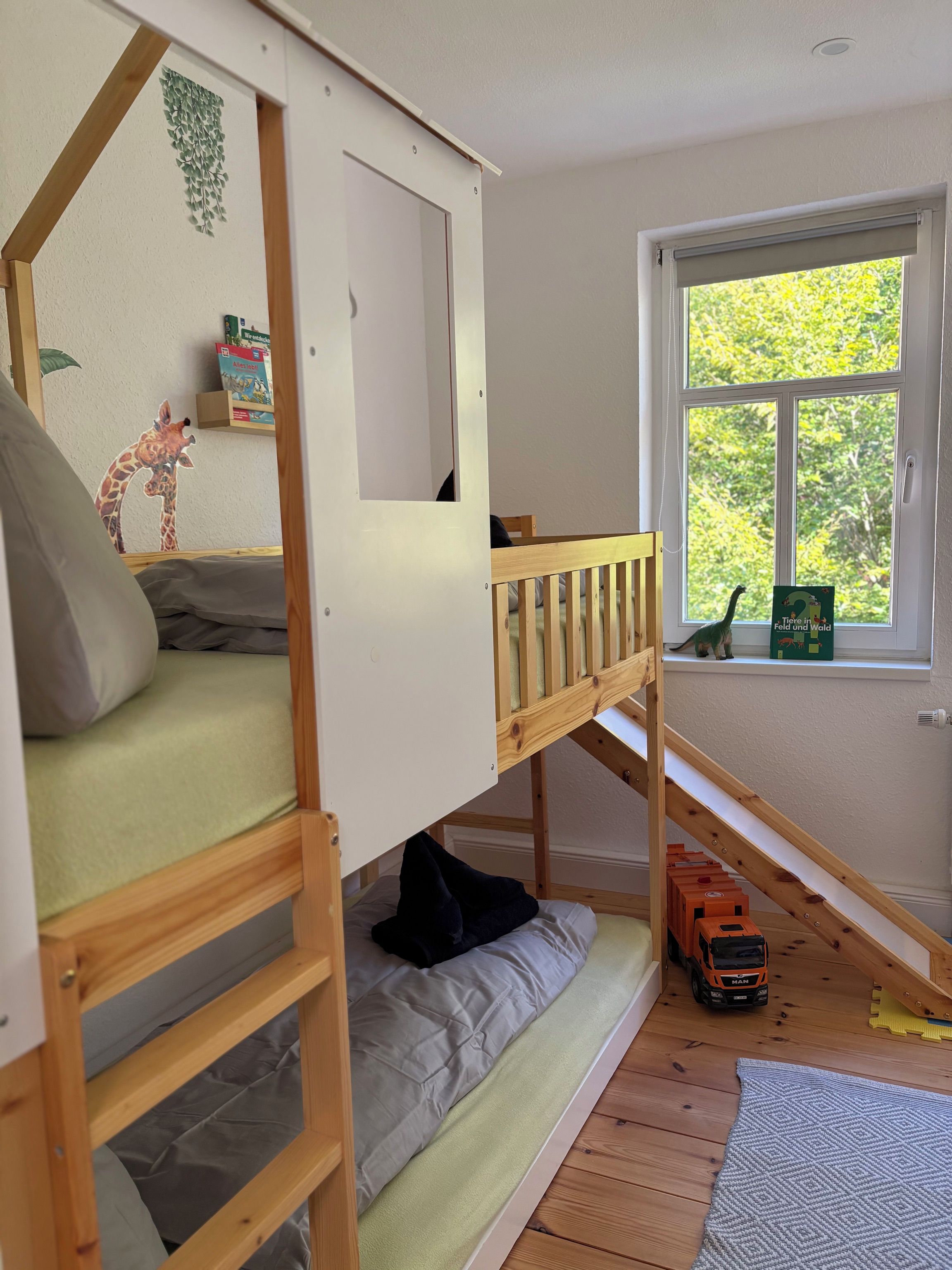 A child's bunk bed with a window view, a toy train, and a giraffe decoration.