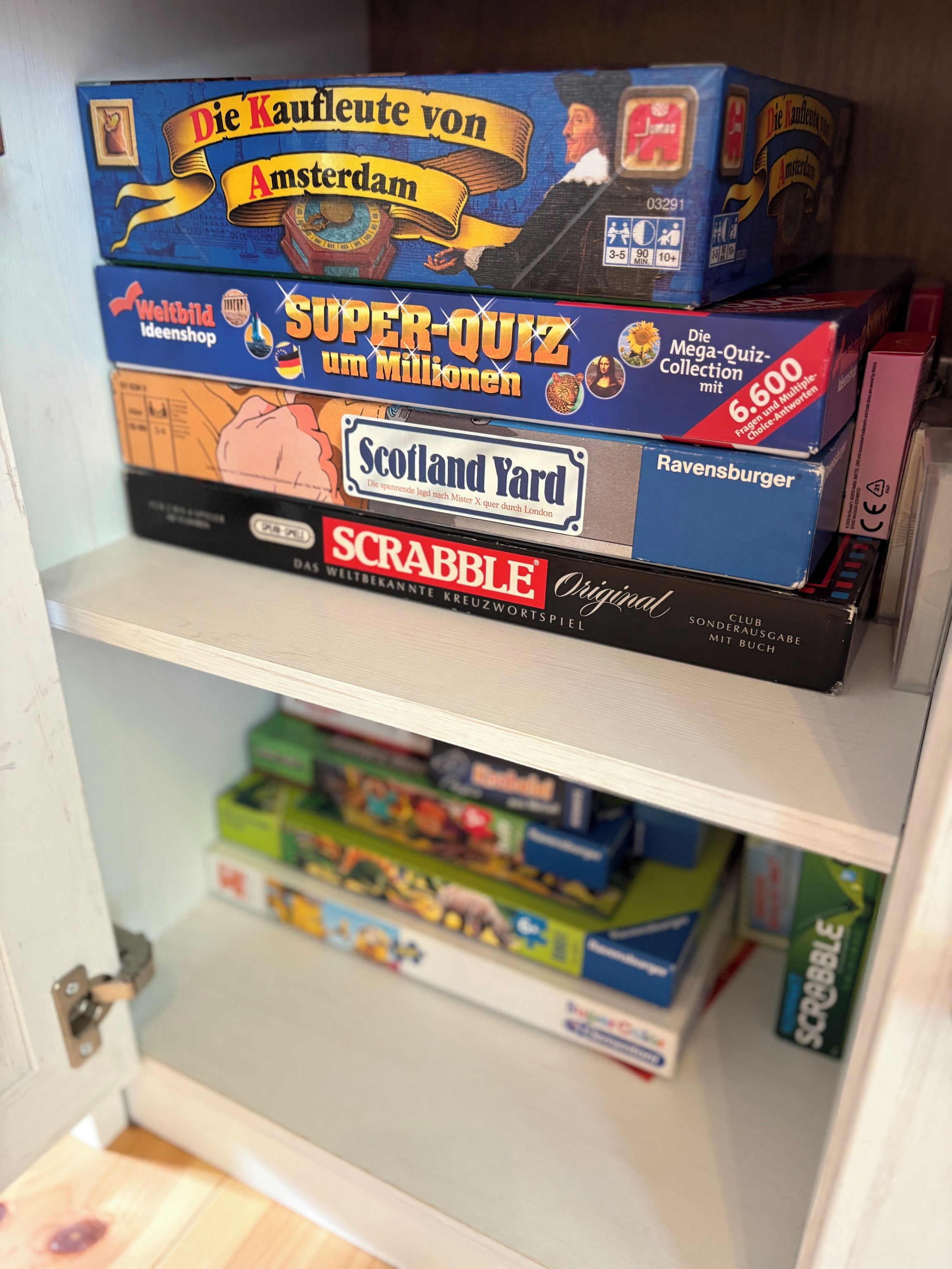 Un estante con diversos juegos de mesa, incluyendo 'Die Kaufleute von Amsterdam' y 'Super-Quiz um Millionen'.