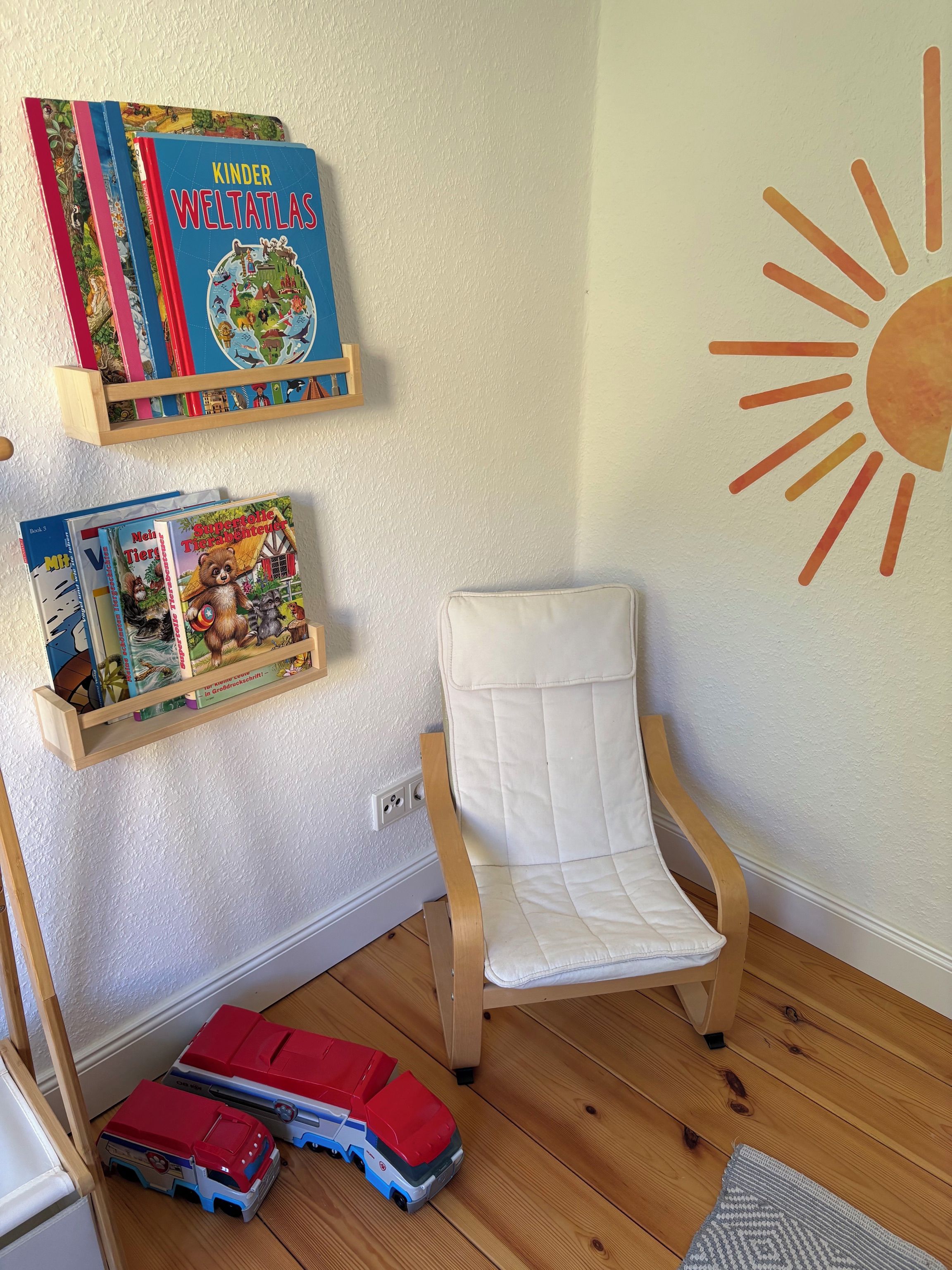 Ein Zimmer mit weißem Stuhl, Holzboden und einer Wand mit Sonnendekoration.