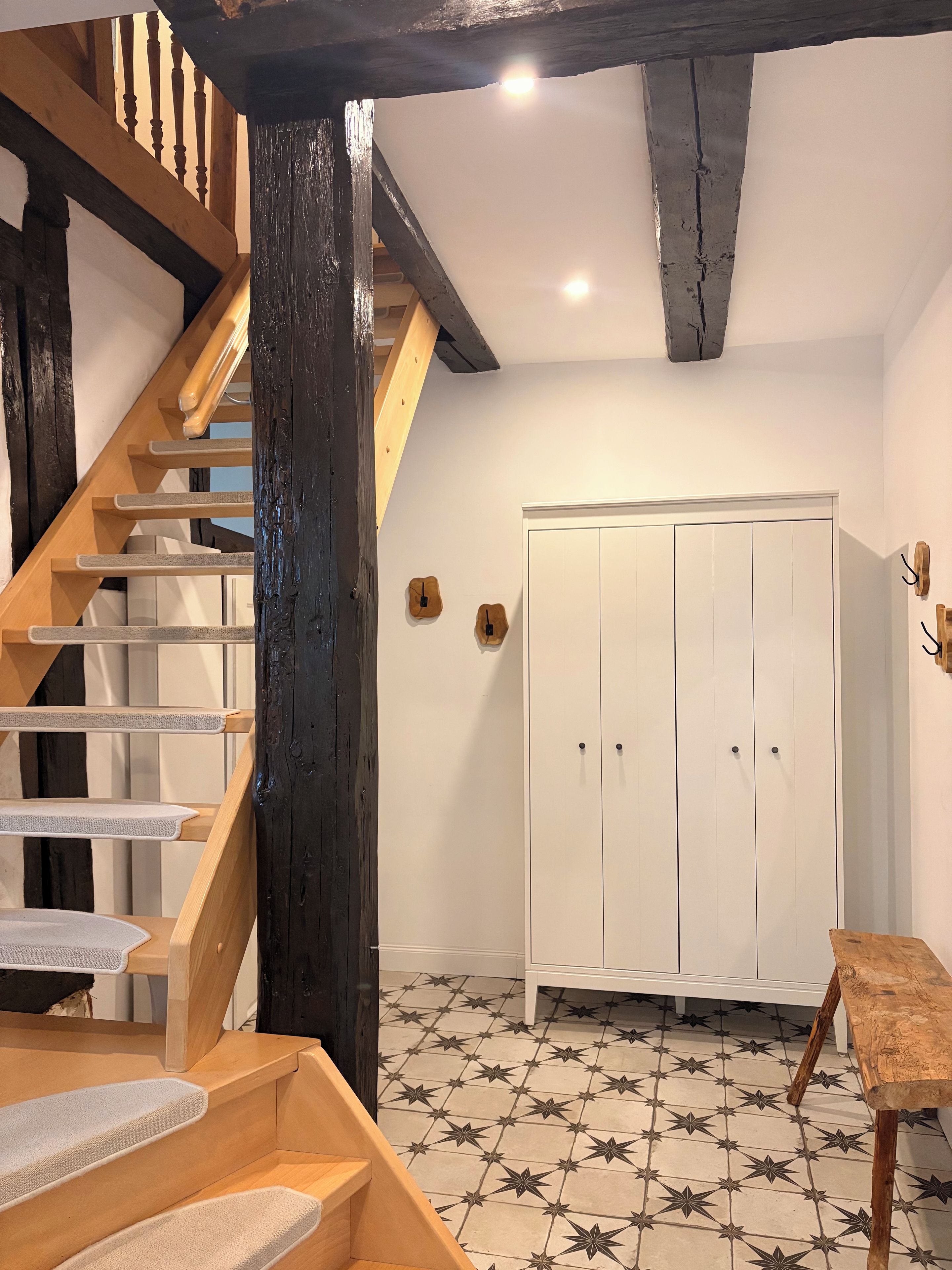 Un escalier avec des marches en bois et une rampe, une armoire blanche à deux portes et un sol carrelé orné d’un motif en étoile.
