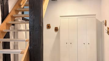 Un escalier avec des marches en bois et une rampe, une armoire blanche à deux portes et un sol carrelé orné d’un motif en étoile.