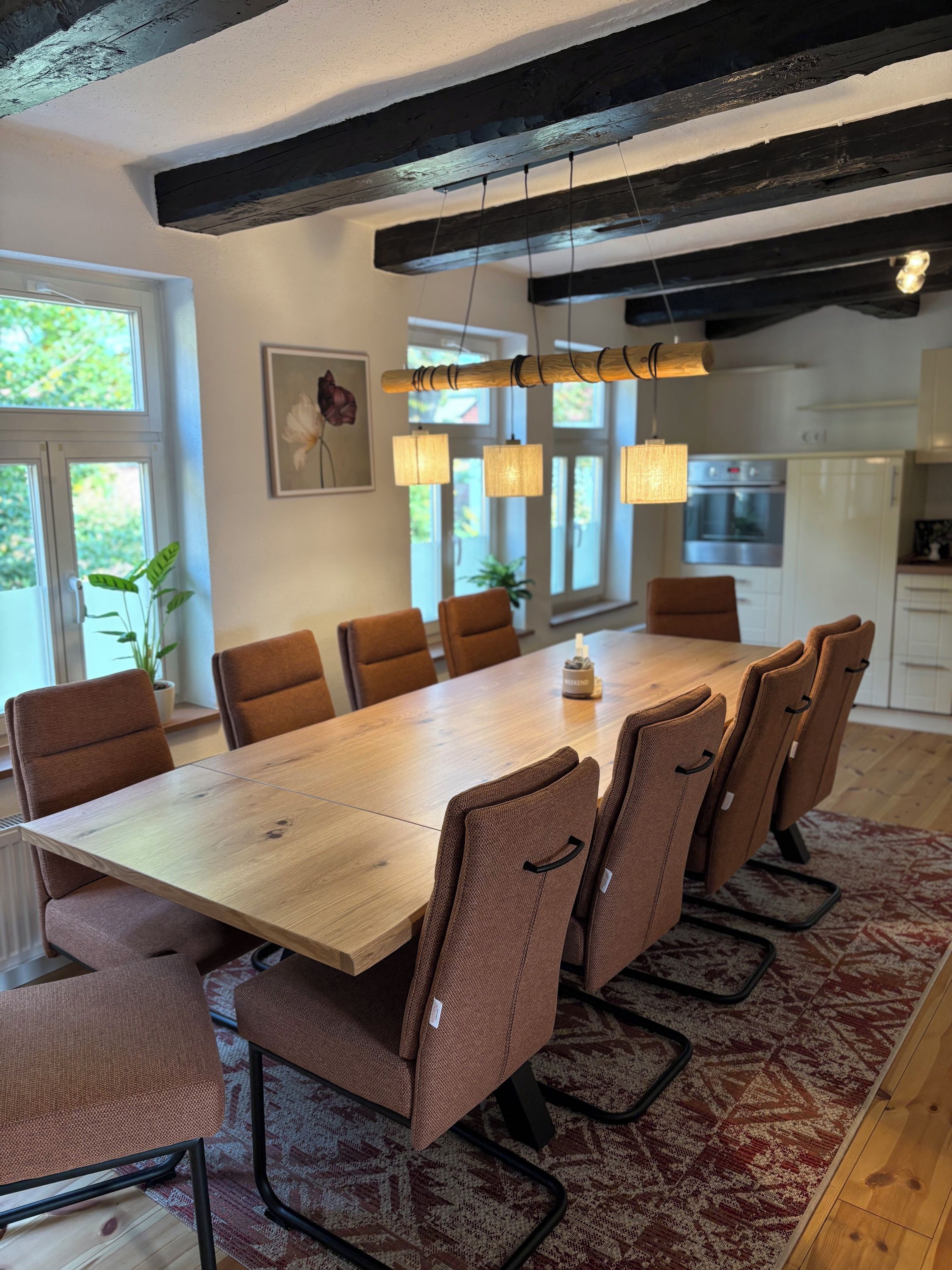 Un comedor con mesa de madera y sillas tapizadas en tonos marrones, un tapete estampado e iluminación colgante.