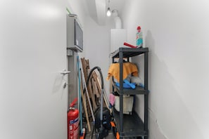 Ein schmaler Gang mit einem Feuerlöscher, Reinigungsausrüstung und einem Regal mit Putzmitteln.