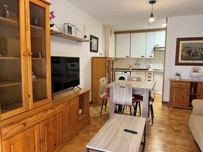 Ein modernes Wohnzimmer mit Holzschrank, Fernseher und Essbereich mit Stühlen und Tisch.