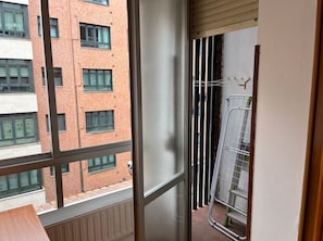 A view from a balcony with a metal railing, a window, and a view of a brick building with multiple windows. - Oviedo 2BR Flat by HUCA Hospital · Sleeps 3 (Oviedo)
