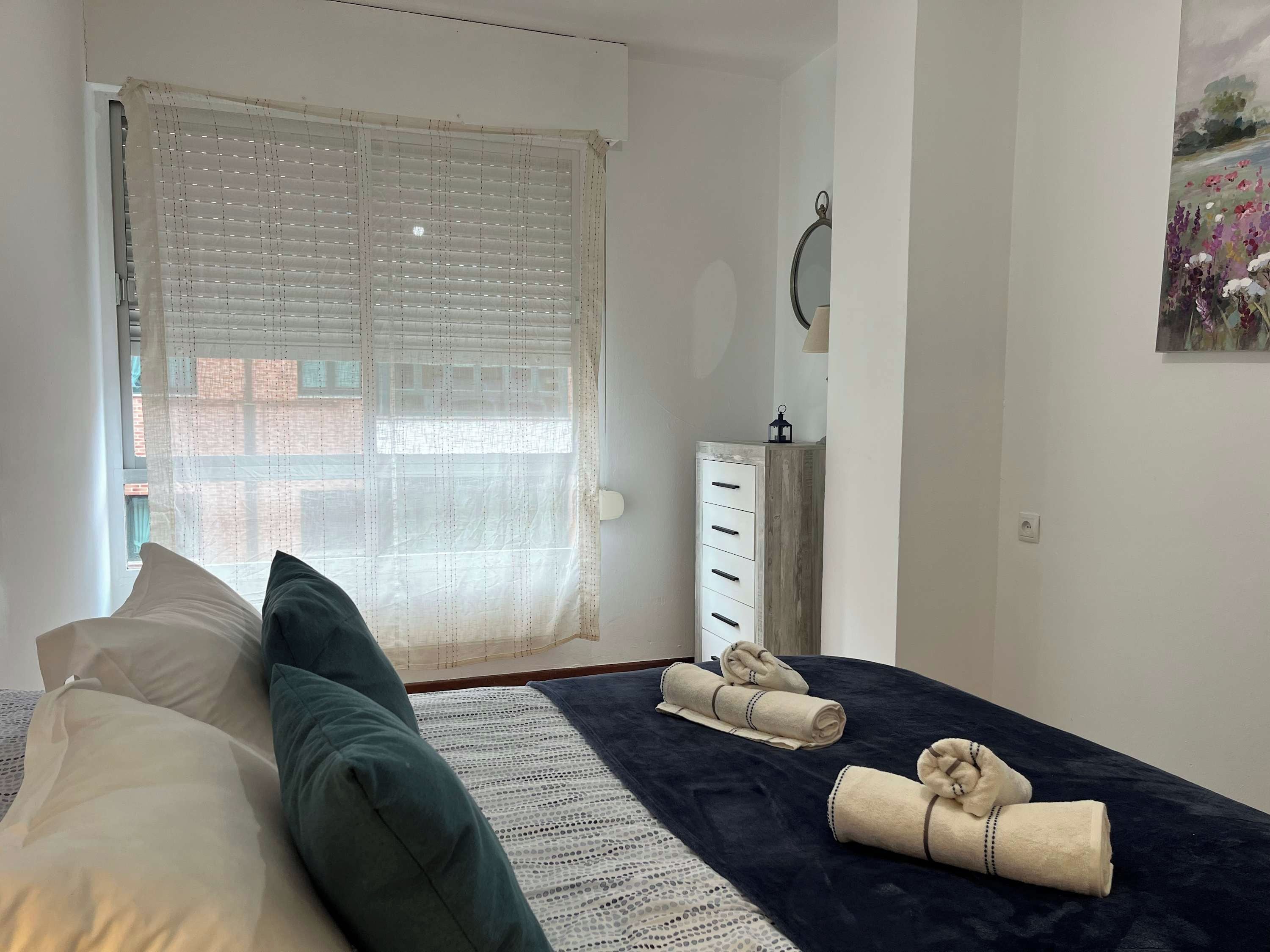 Une chambre à coucher avec un lit, des oreillers, une table de chevet avec une lampe, une armoire et un tableau accroché au mur.