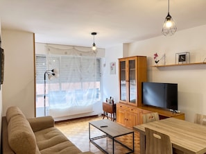 A living room with a sofa, a coffee table, a TV, a cabinet, and a hanging light fixture. - Oviedo 2BR Flat by HUCA Hospital · Sleeps 3 (Oviedo)