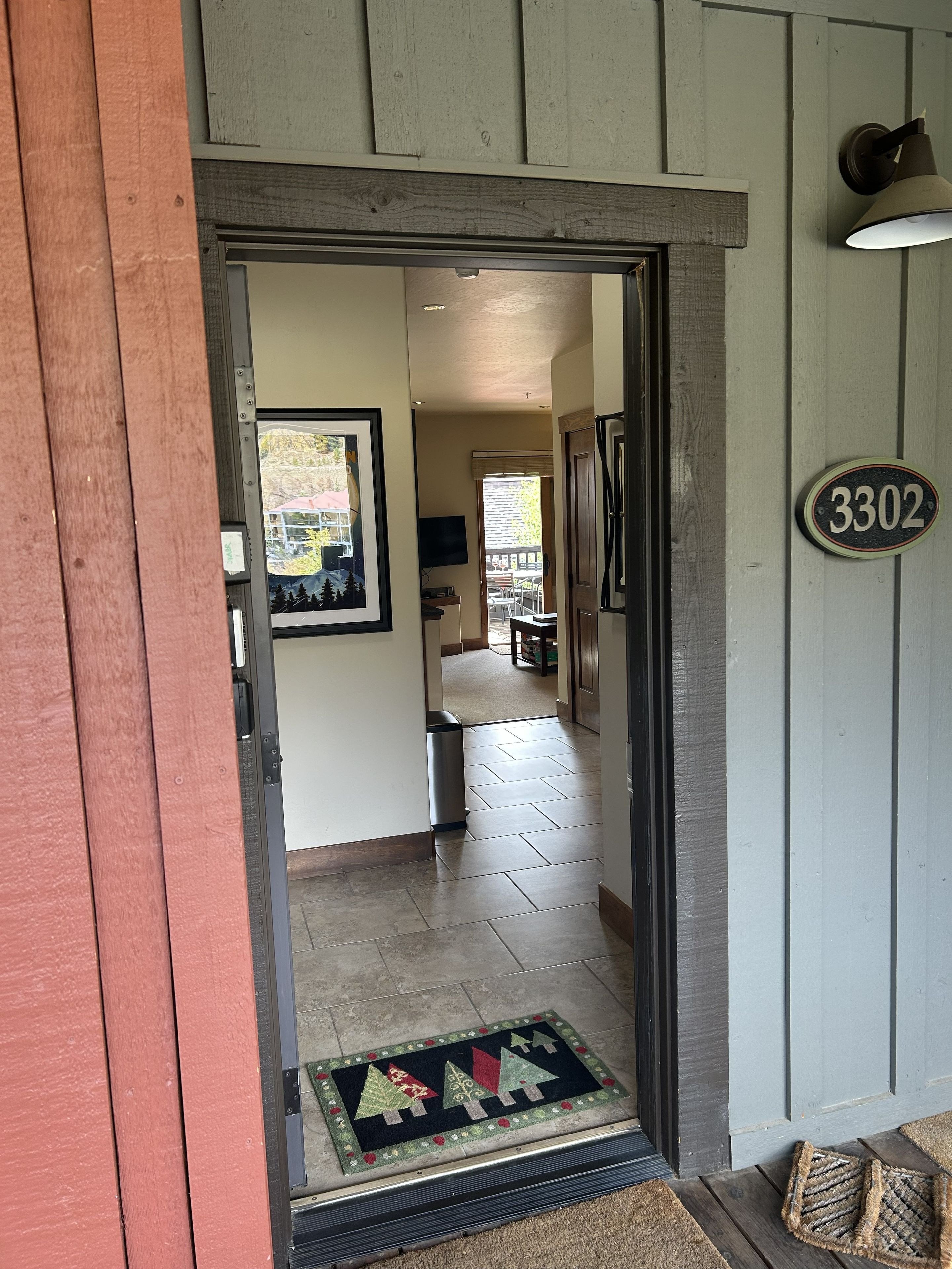A wooden door with a number plate, a doormat with a Christmas tree design, and a hallway leading to a dining area.