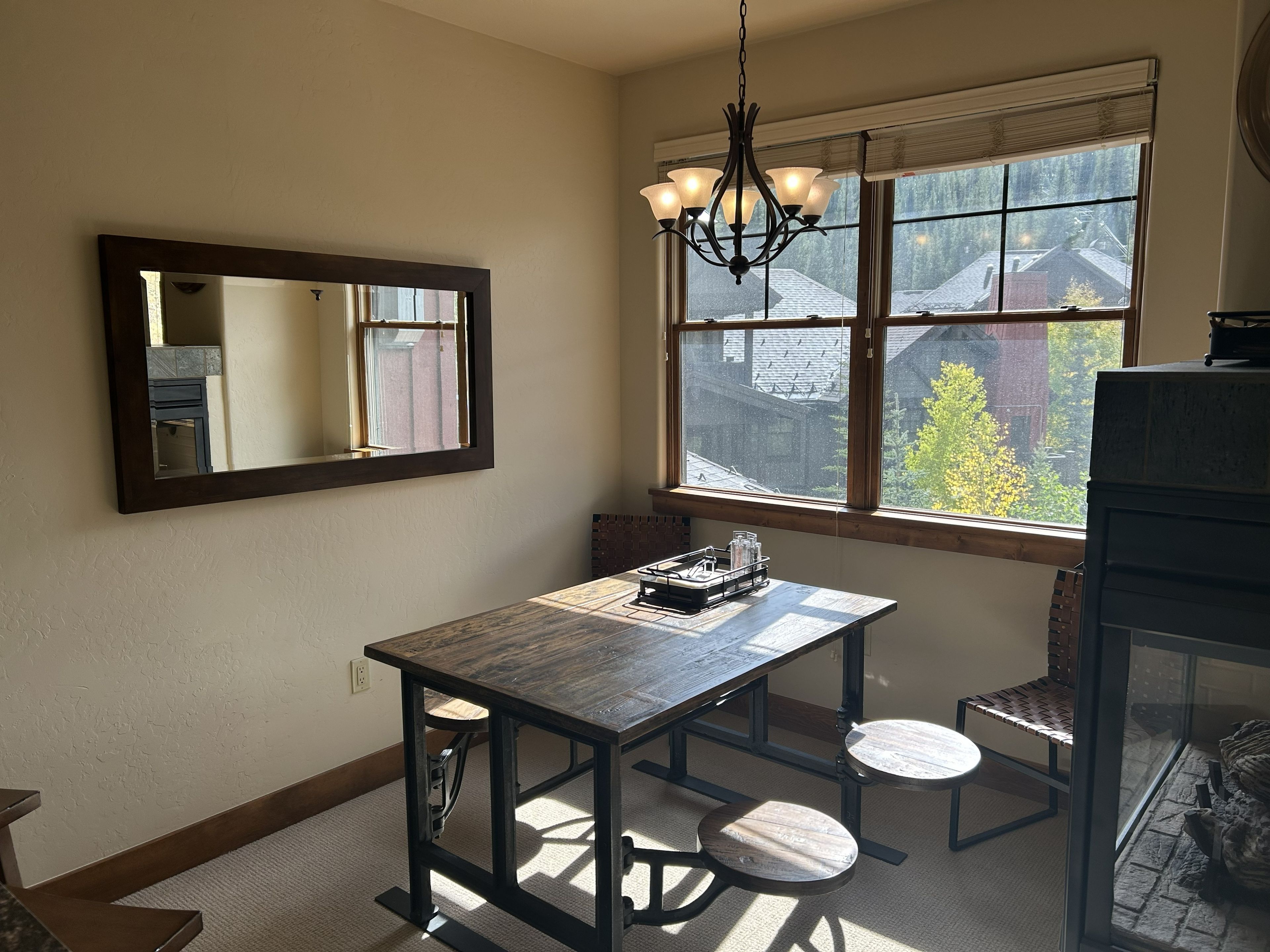 A dining area with a table and chairs, a chandelier, a window with a view, and a mirror on the wall.
