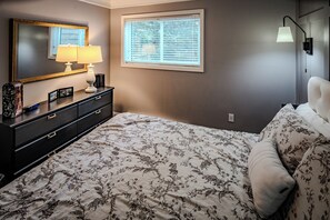 Ein Schlafzimmer mit Bett, Kommode, Lampe und Fenster.