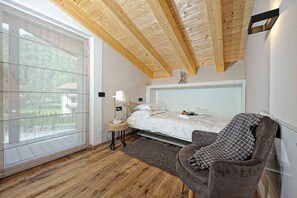 Un dormitorio con cama, mesita de noche, lámpara, silla y un ventanal grande.