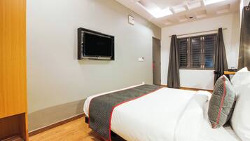 Une chambre d’hôtel avec un lit, un téléviseur fixé au mur, une fenêtre avec des rideaux et un plancher en bois.