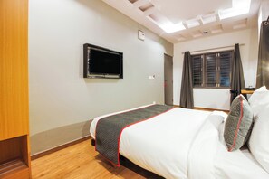 A hotel room with a bed, a television mounted on the wall, a window with curtains, and a wooden floor.