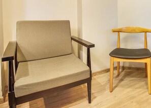 A chair with a dark frame and a cushion, positioned next to a wooden chair with a light-colored seat. - Super Townhouse RCC Sunrise (Hyderabad)