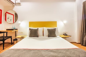 Una habitación de hotel con cama, mesitas de noche, escritorio, silla, espejo y teléfono.