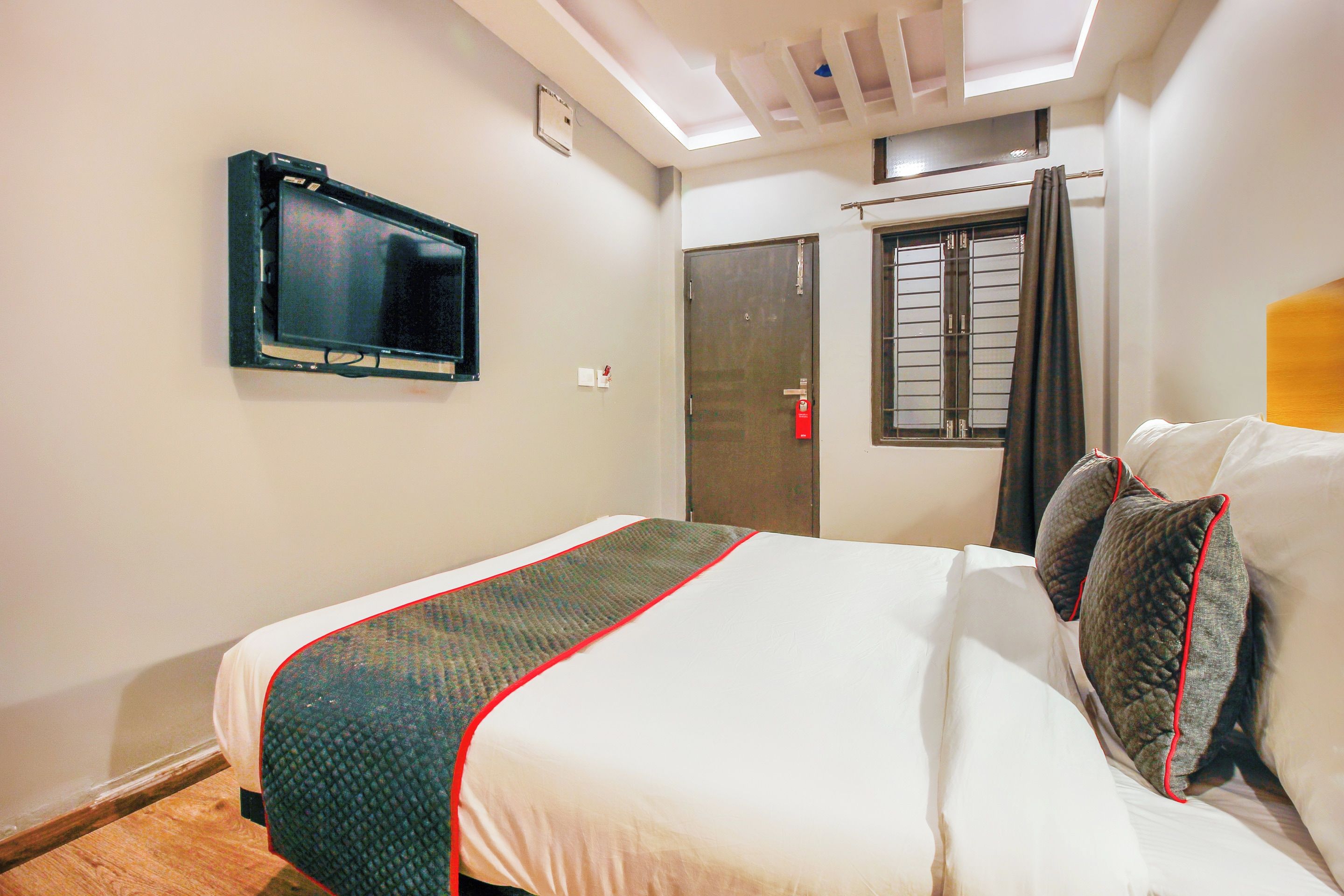 A hotel room with a bed, a television mounted on the wall, a window with curtains, and a door.