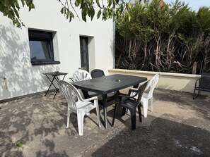 Un patio exterior con una mesa y sillas, una ventana pequeña y una pared con un árbol.
