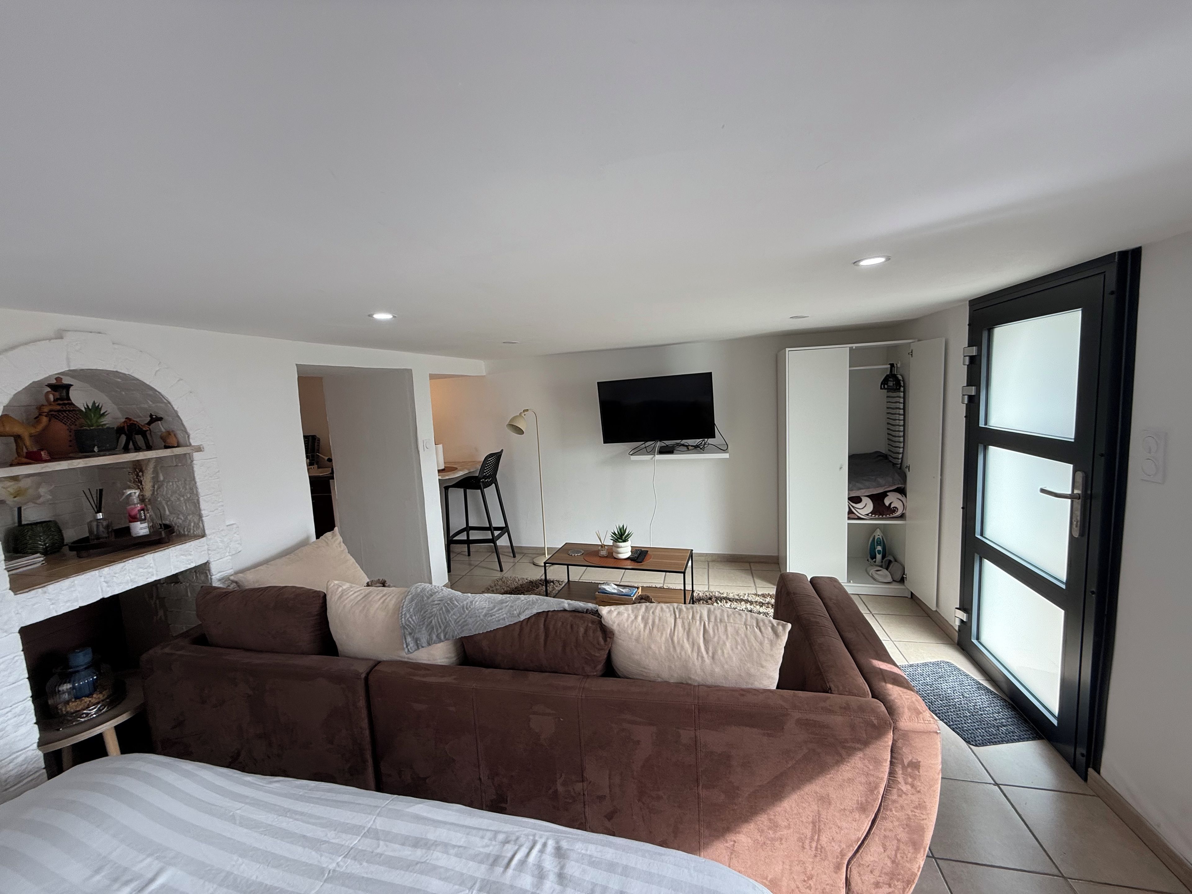 A modern living room with a brown sofa, a flat-screen TV mounted on the wall, and a dining area with a small table and chairs.