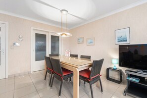 Ein Essbereich mit einem Glastisch, Korbstühlen, einem Fernseher und Kunstwerken an der Wand.