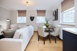 A modern living room with a sofa, dining table, chairs, and a vase with plants. - A Little Navy Number Islington (London)