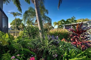 A lush garden with various plants and trees, a clear blue sky, and a building in the background. - Bring your boat and enjoy Southwest Florida from your own backyard. Royal Palm features a private dock and boat lift available for guest use, with canal access leading toward Charlotte Harbor and the Gulf of Mexico. (Port Charlotte)