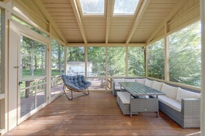 A covered outdoor seating area with a wooden deck, a cushioned chair, a table, and a sofa. - Screened Porch & Steps to Lake! Pocono Summit Home (Pocono Summit)