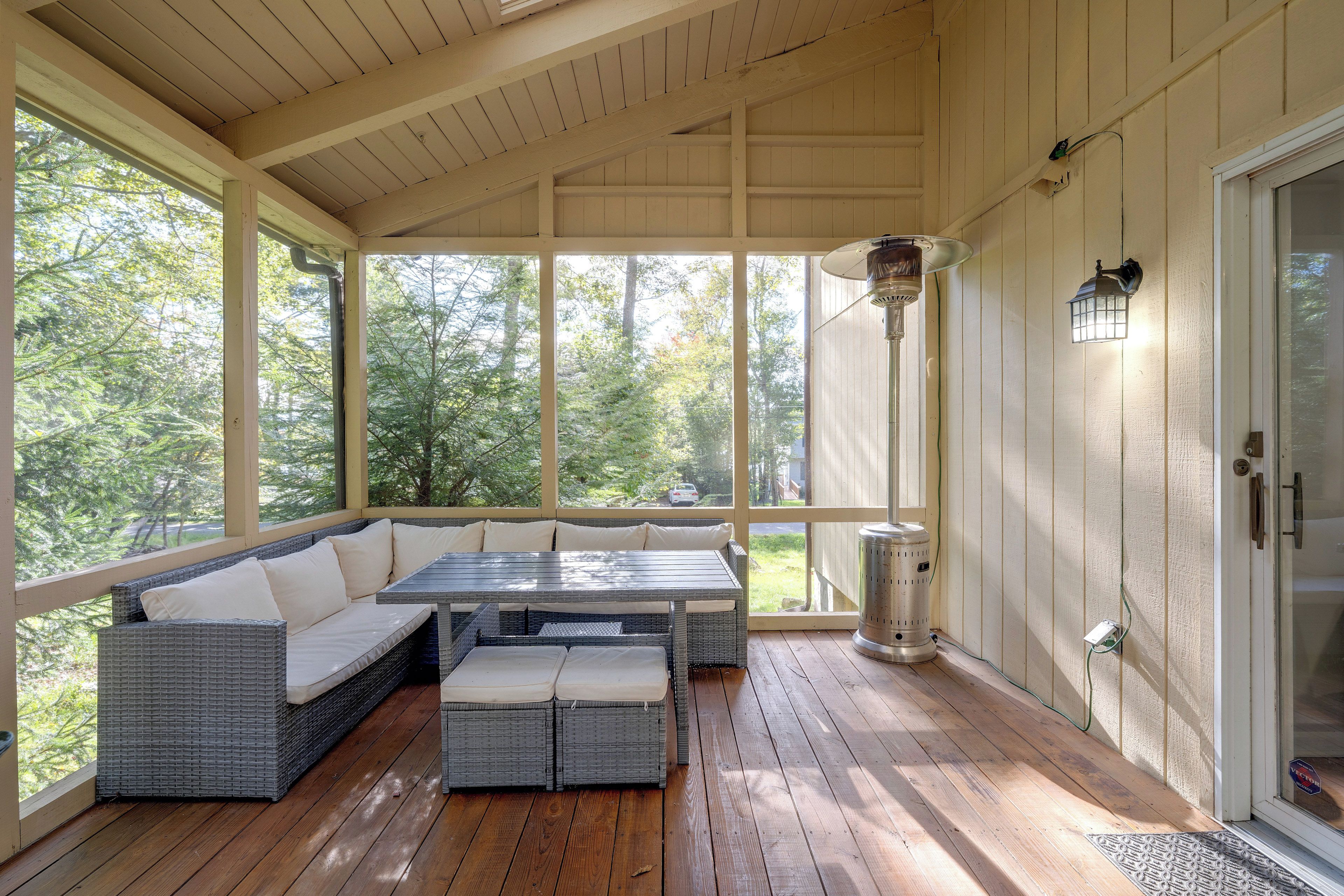 A covered porch with a cushioned seating area, a table, and a heater.
