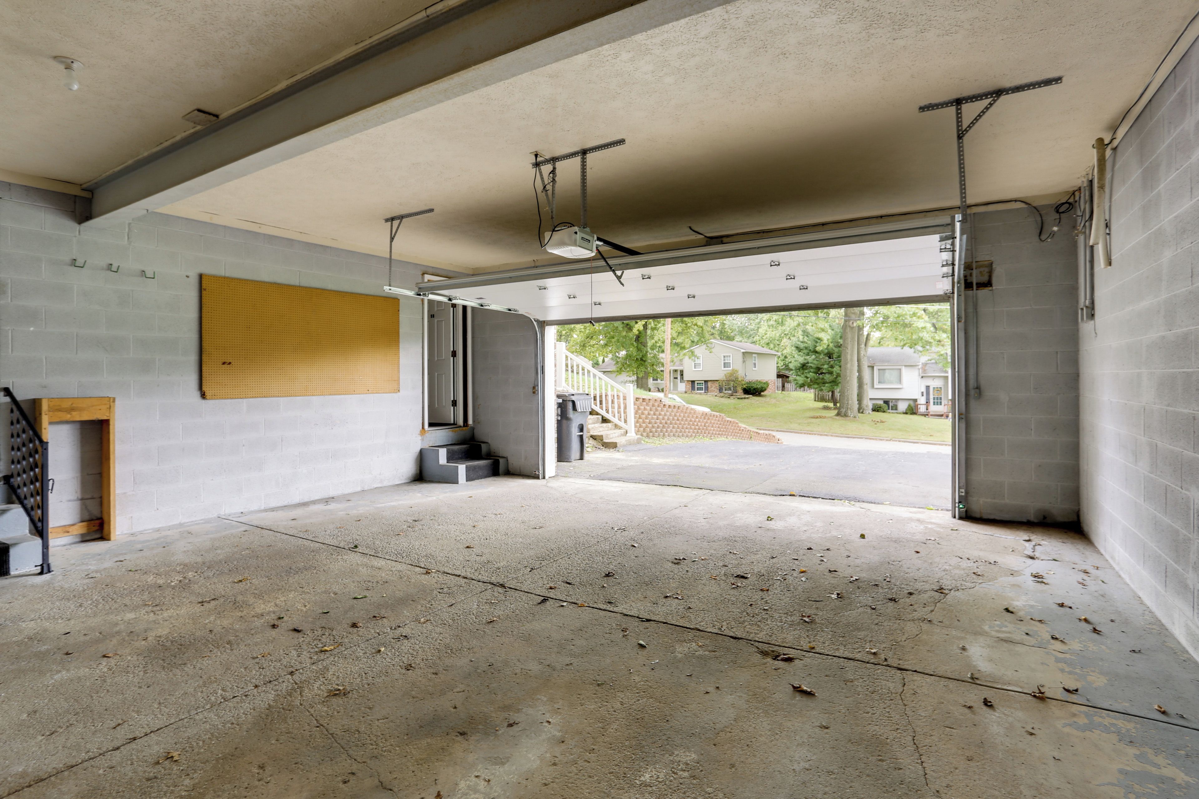 An open garage with a concrete floor, a pegboard on the wall, and a staircase leading outside.