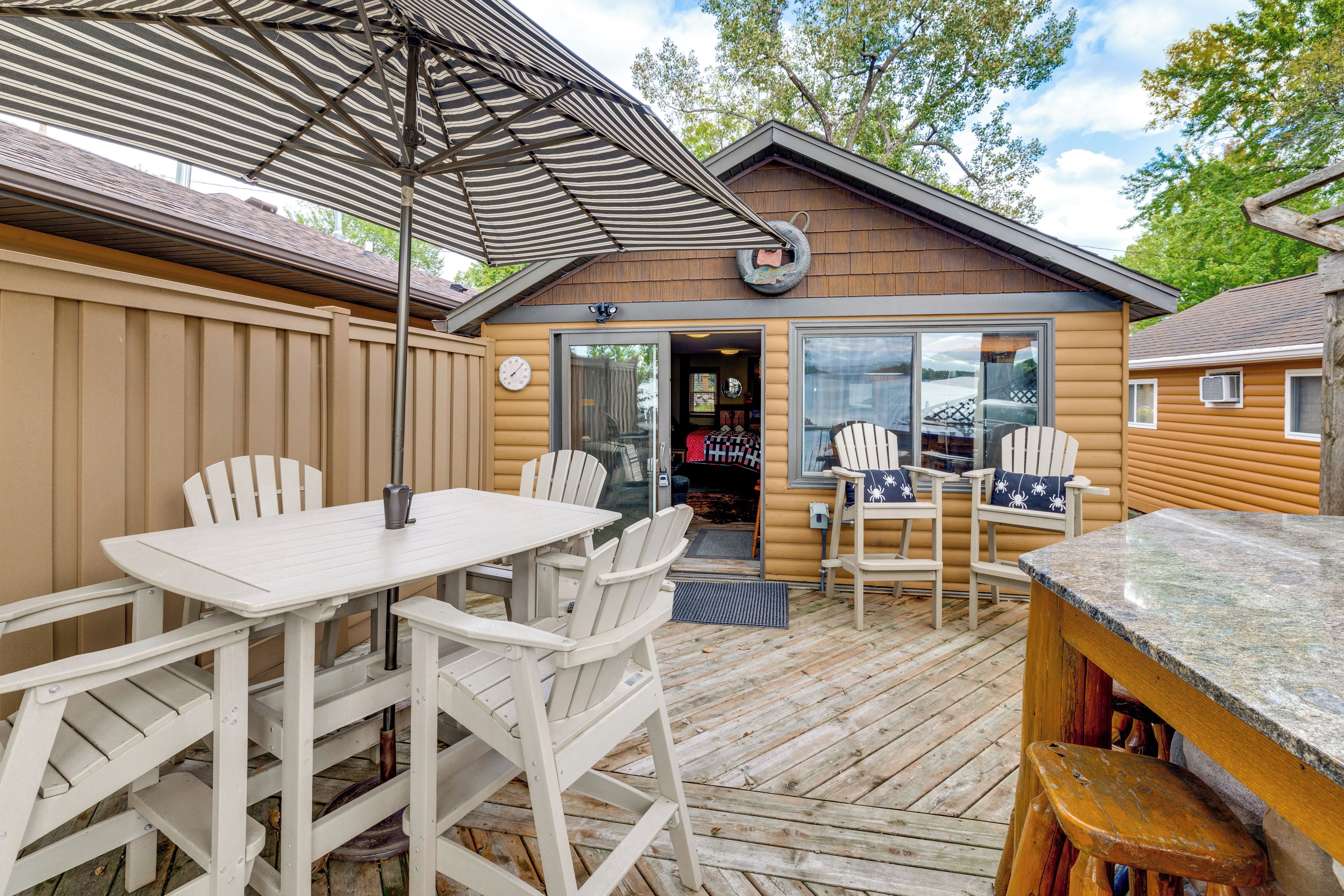 A wooden deck with a table and chairs, a covered area with striped fabric, and a building entrance with a door and windows.