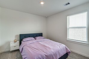 Ein Schlafzimmer mit einem Bett, einem Nachttisch, einem Fenster mit Jalousien und einer Deckenleuchte.