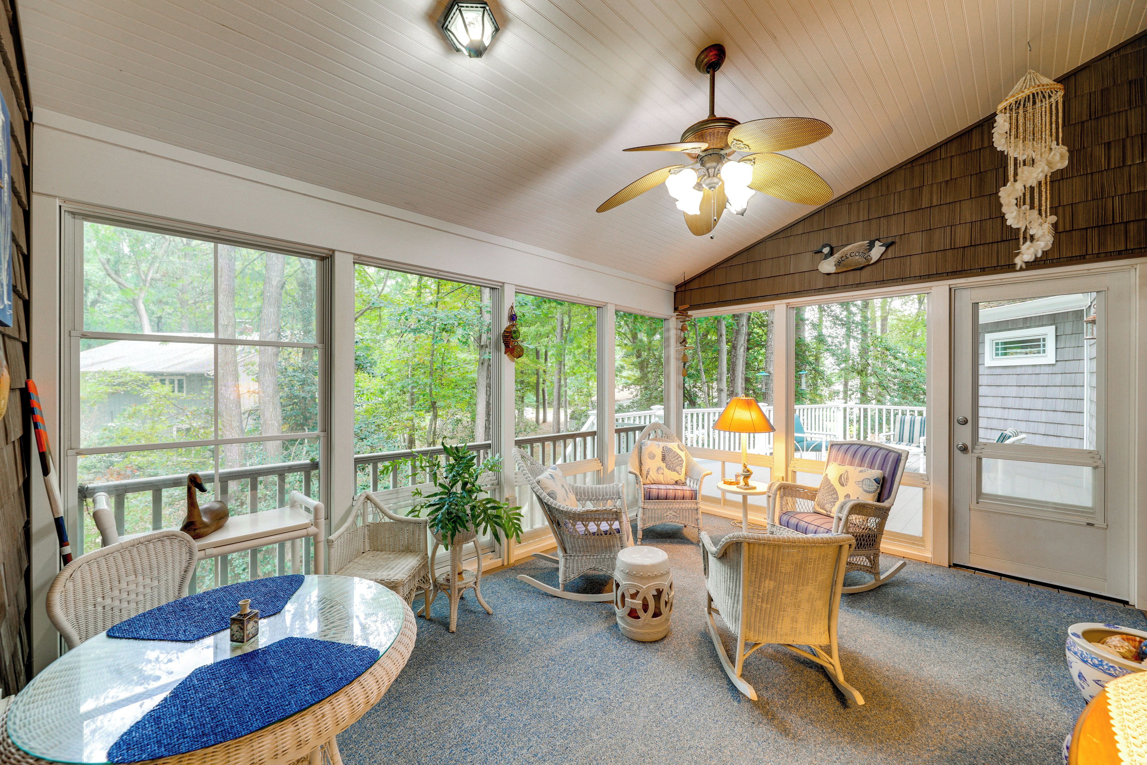 A sunroom with wicker furniture, large windows, and a ceiling fan.