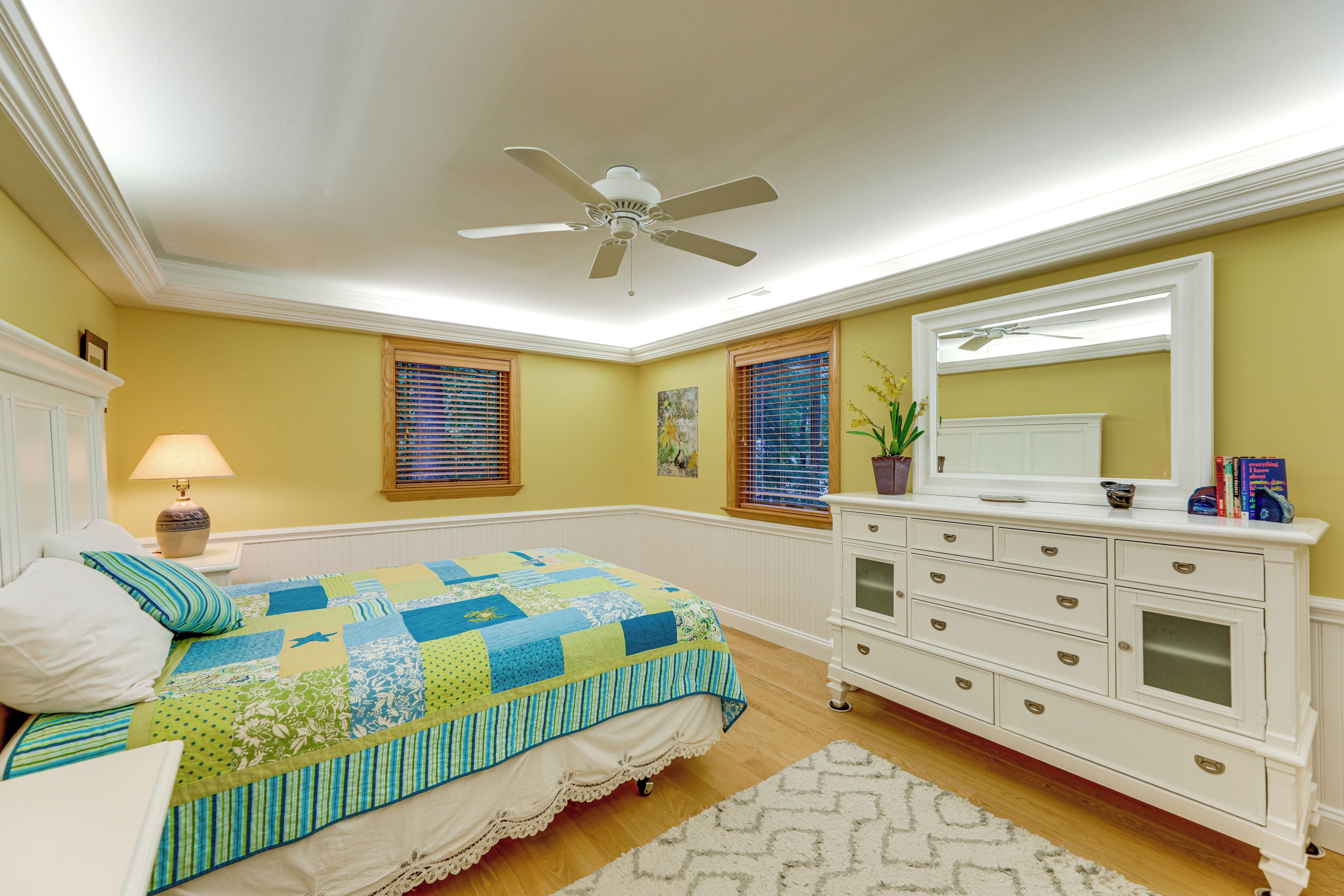 A bedroom with a bed, dresser, ceiling fan, and a window with blinds.