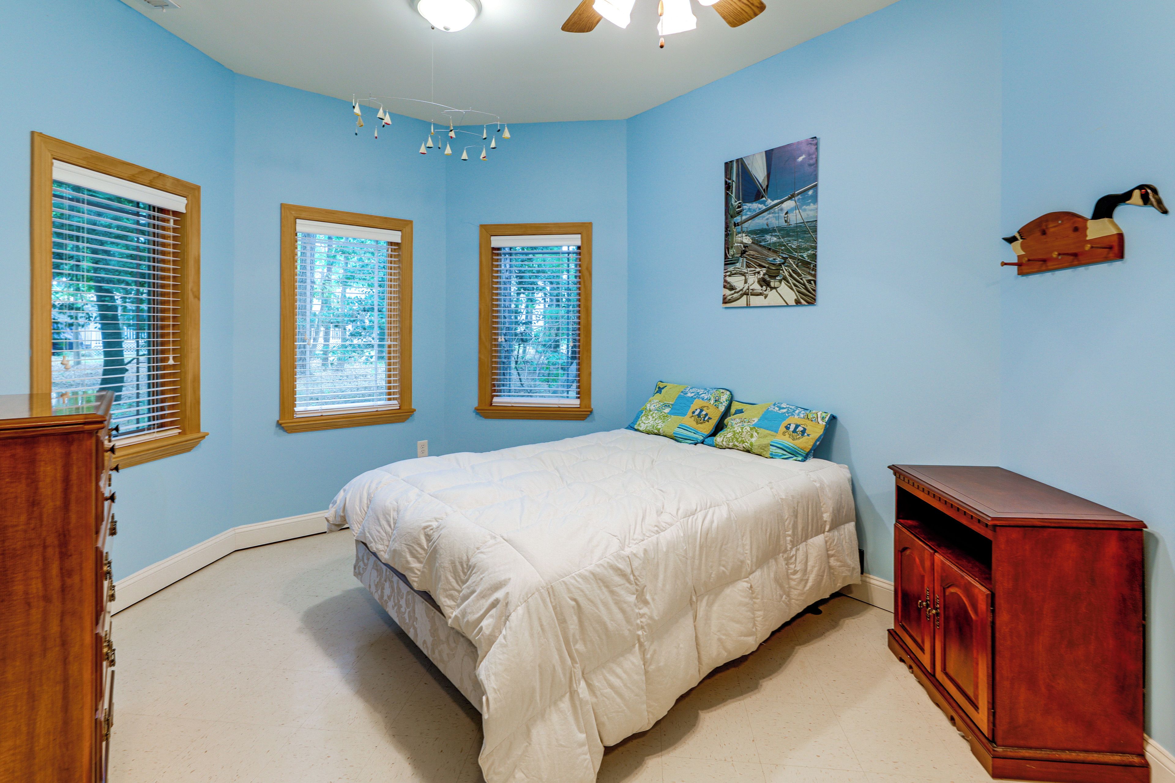 A bedroom with a bed, a wooden cabinet, and three windows with blinds.
